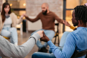 Group of young people holding hands and praying, sitting all together on group therapy in circle.