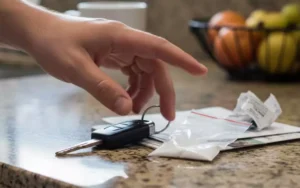 A hand reaches for car keys beside a small plastic bag containing white powder on a kitchen counter, symbolizing the hidden risks of casual cocaine use