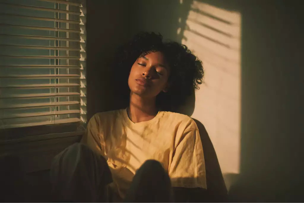 A young woman sits quietly by a sunlit window